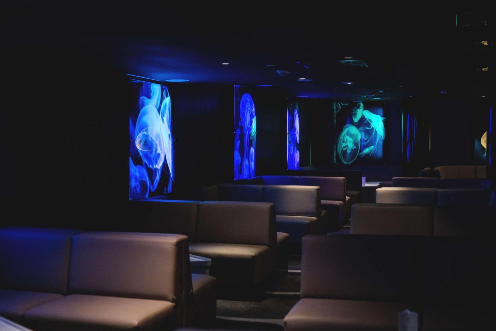 Radisson Blu Resort Swinoujscie Ngoại thất bức ảnh The photo shows a dimly lit interior space, likely a lounge or a seating area. The walls are adorned with glowing blue and turquoise images, possibly of jellyfish or abstract aquatic forms, creating an ambient atmosphere. There are several upholstere