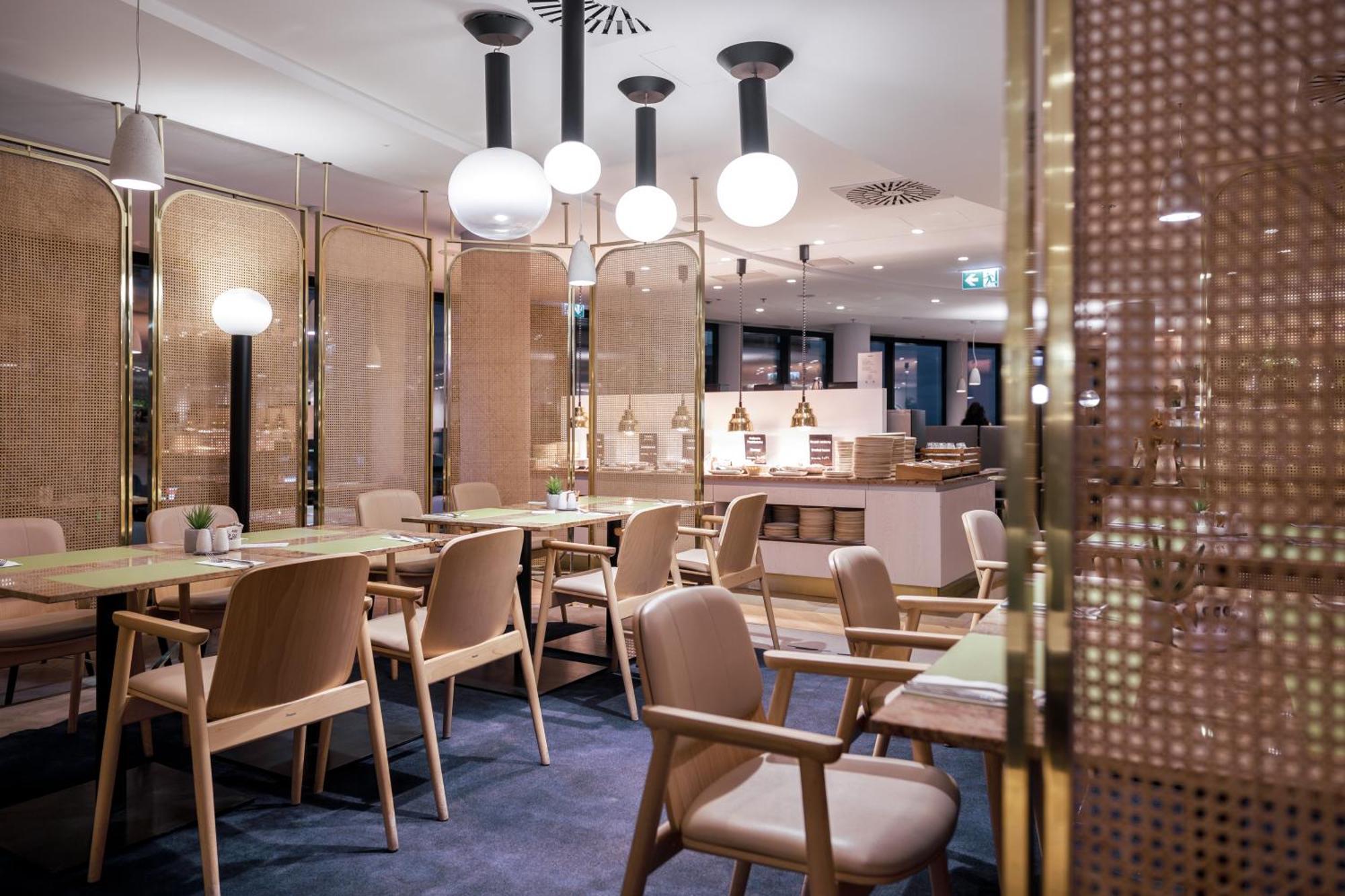 Radisson Blu Resort Swinoujscie Ngoại thất bức ảnh The photo shows a modern restaurant interior. There are wooden tables and chairs arranged neatly. The atmosphere appears warm and inviting, with soft lighting provided by round pendant lamps hanging from the ceiling. Partitions made of woven material