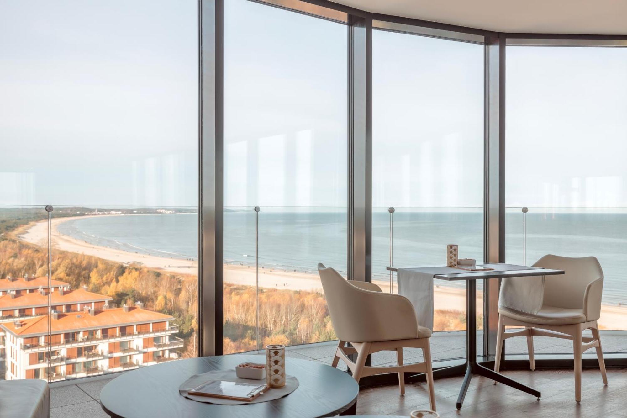 Radisson Blu Resort Swinoujscie Ngoại thất bức ảnh The photo shows a modern interior space with large floor-to-ceiling windows that provide a stunning view of the beach and sea. The area appears to be a dining or lounge space, featuring a minimalistic table and chairs. There is a sense of tranquility
