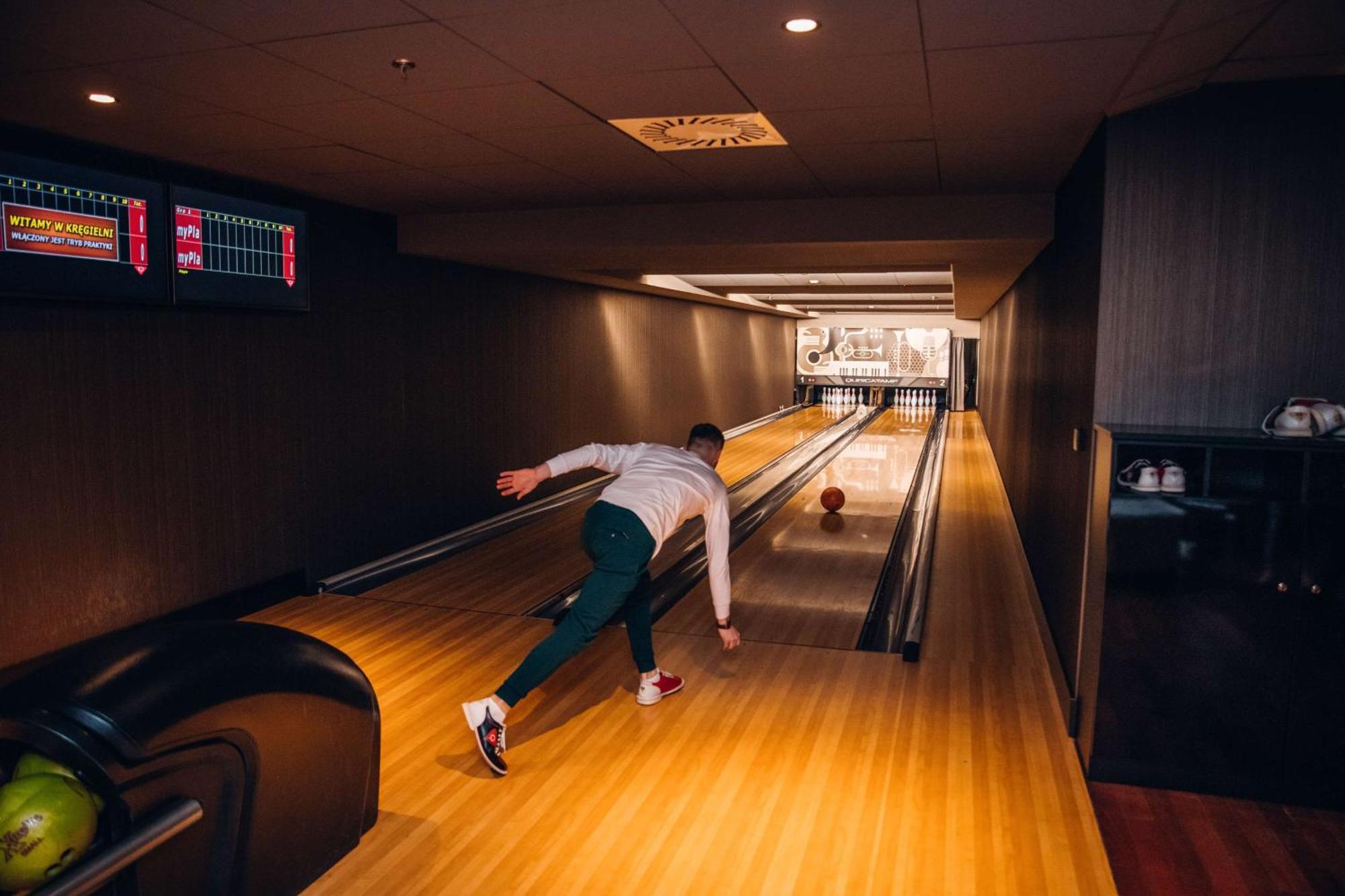 Radisson Blu Resort Swinoujscie Ngoại thất bức ảnh The photo shows a bowling alley. In the foreground, a person is throwing a bowling ball down the lane. They are wearing a white top and green pants, with red and white shoes. The bowling lane is made of polished wood, and at the end of the lane, ther