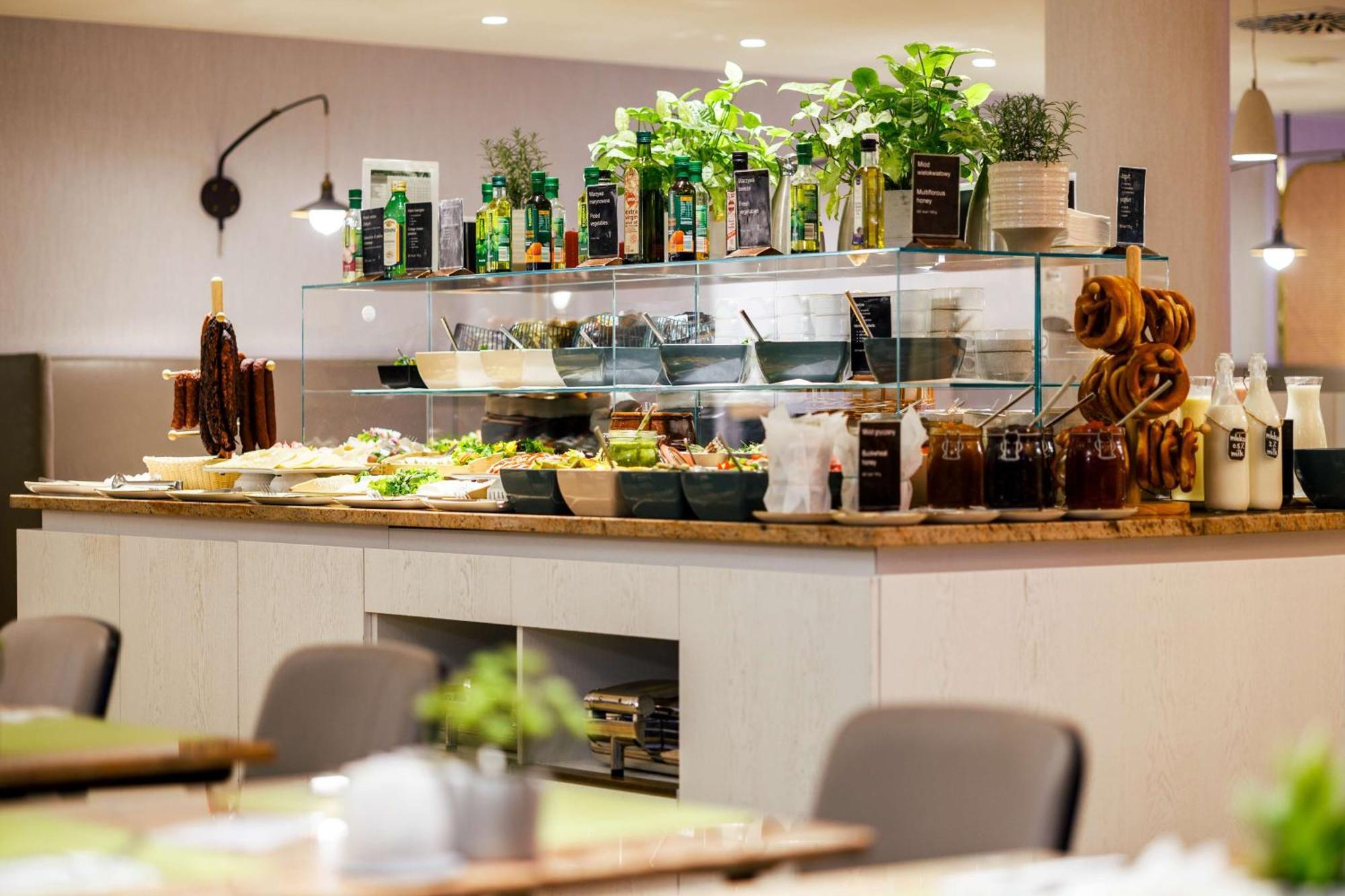 Radisson Blu Resort Swinoujscie Ngoại thất bức ảnh The photo shows a well-organized buffet display in a restaurant setting. There is a glass counter filled with various dishes. On the upper shelf, there are several bottles of oil and herbs, indicating a focus on fresh and healthy ingredients. Below t