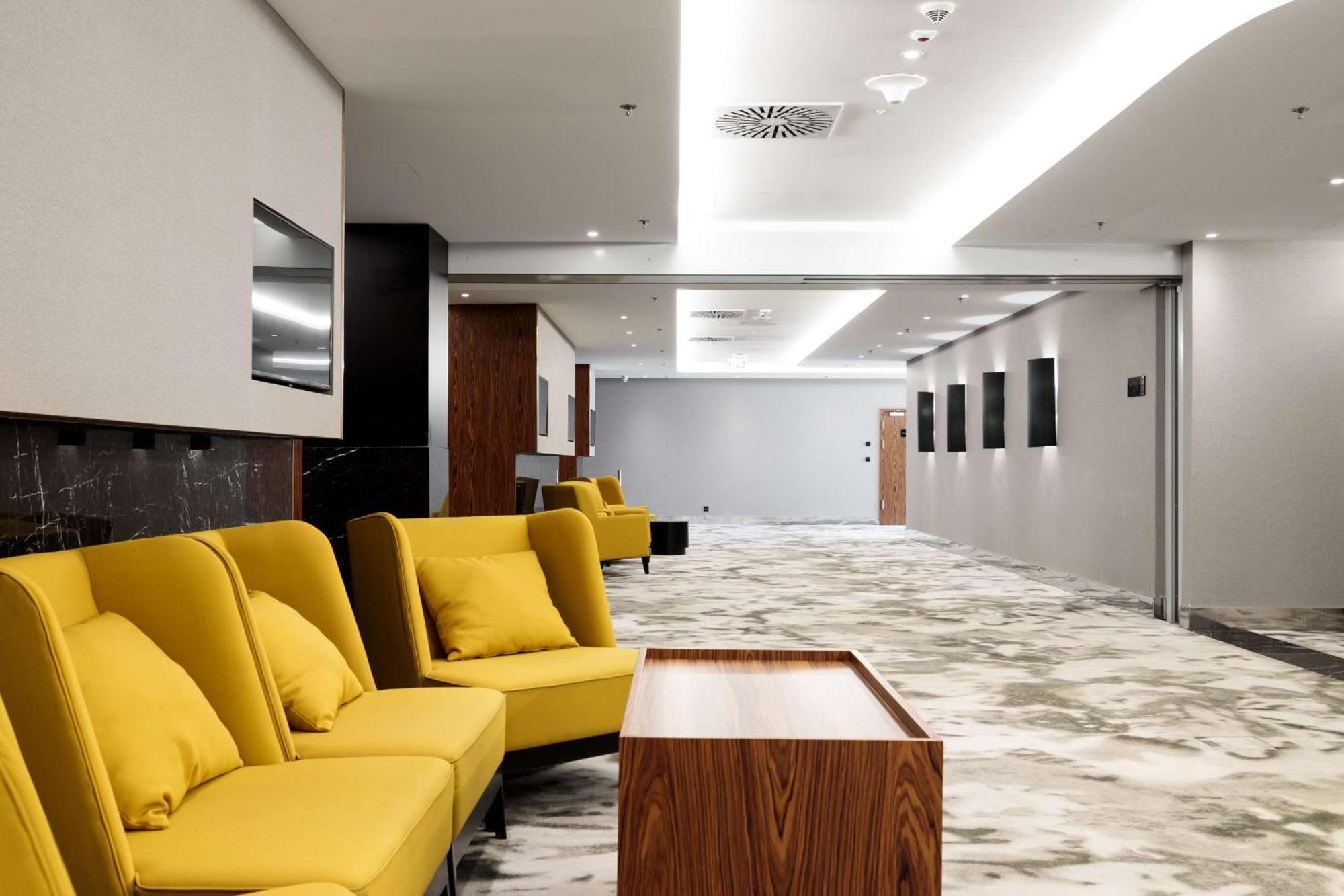 Radisson Blu Resort Swinoujscie Ngoại thất bức ảnh The photo shows a modern interior space, likely a lobby or waiting area. There are several yellow sofas with cushions arranged in a casual seating area. In front of the sofas, there is a wooden coffee table. The flooring features a gray and white mar