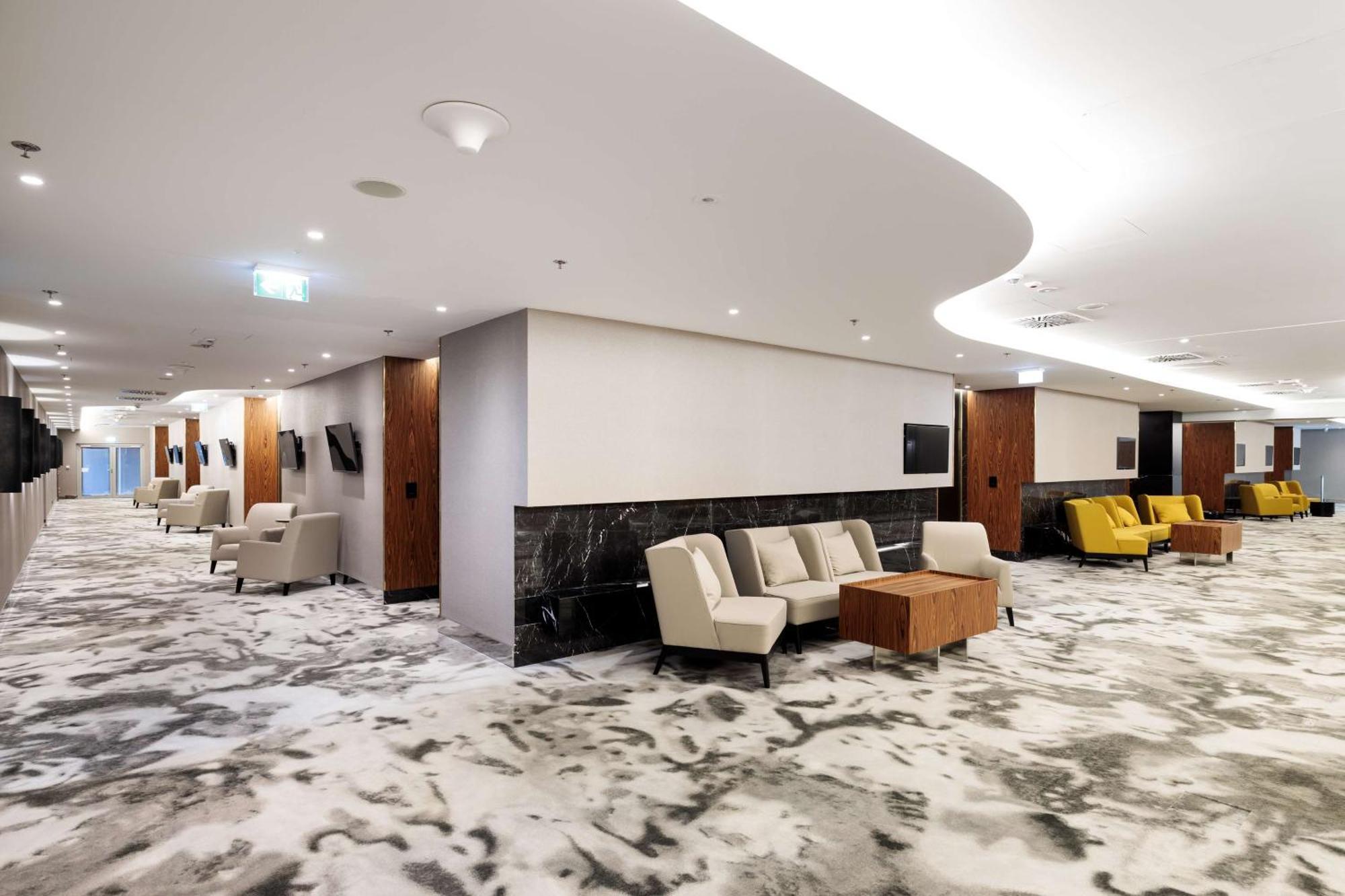 Radisson Blu Resort Swinoujscie Ngoại thất bức ảnh The photo shows a modern interior space, likely a lobby or lounge area. The flooring features a patterned carpet, and the walls are neutral in color, creating a calm ambiance. There are comfortable seating arrangements, including a group of beige cha