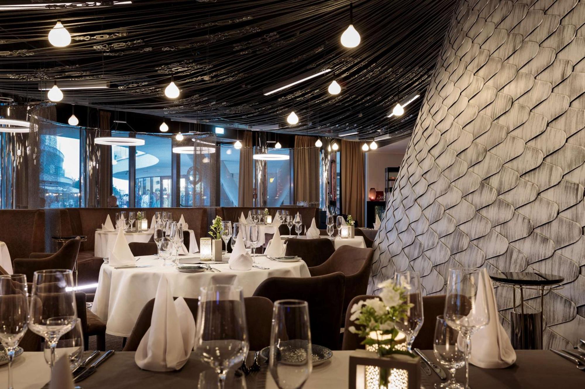 Radisson Blu Resort Swinoujscie Ngoại thất bức ảnh The photo shows a stylish restaurant interior. The dining area features elegantly set tables with white tablecloths, glassware, and folded napkins. There are decorative elements like small floral arrangements on the tables. The ceiling is adorned wit