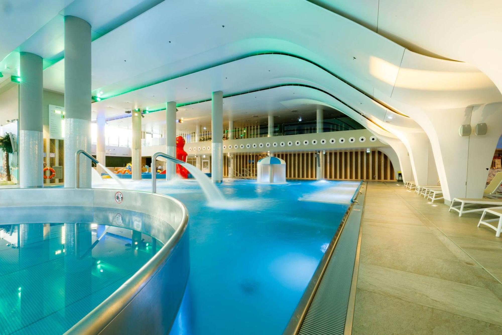 Radisson Blu Resort Swinoujscie Ngoại thất bức ảnh The photo shows a modern indoor swimming pool area with an elegant design. The pool features curved edges and is filled with clear, blue water. There are various amenities, such as jets for relaxation and possibly seating areas along the edges. The l