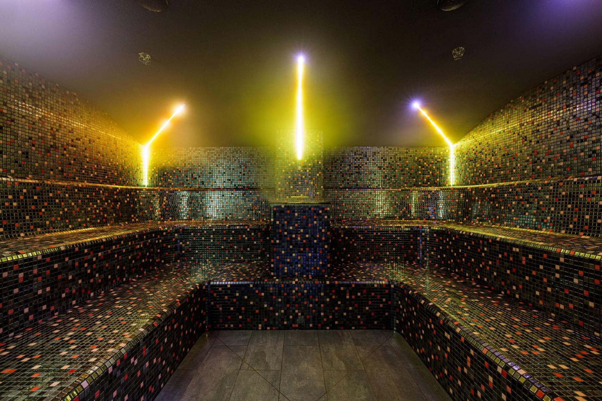 Radisson Blu Resort Swinoujscie Ngoại thất bức ảnh The photo shows the interior of a steam room or sauna. The space is characterized by a series of benches that are built into the walls, allowing for multiple seating options. The walls are adorned with a mosaic of small, colorful tiles that create a 