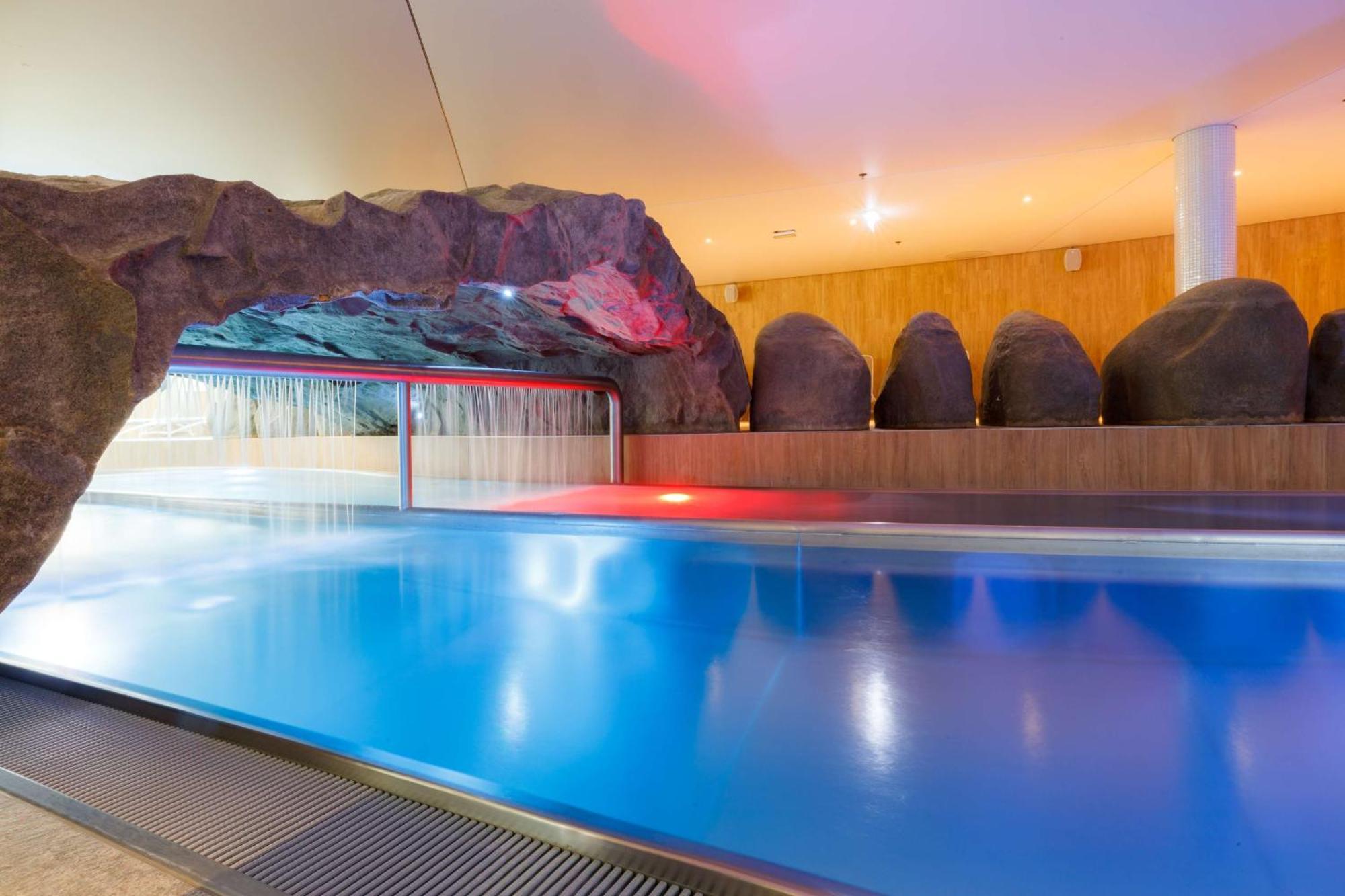 Radisson Blu Resort Swinoujscie Ngoại thất bức ảnh The photo shows a serene indoor swimming pool area. The pool has clear blue water, and there is a distinctive rock formation that resembles a cave on one side. Soft lighting enhances the atmosphere, casting a gentle glow across the space. In the back