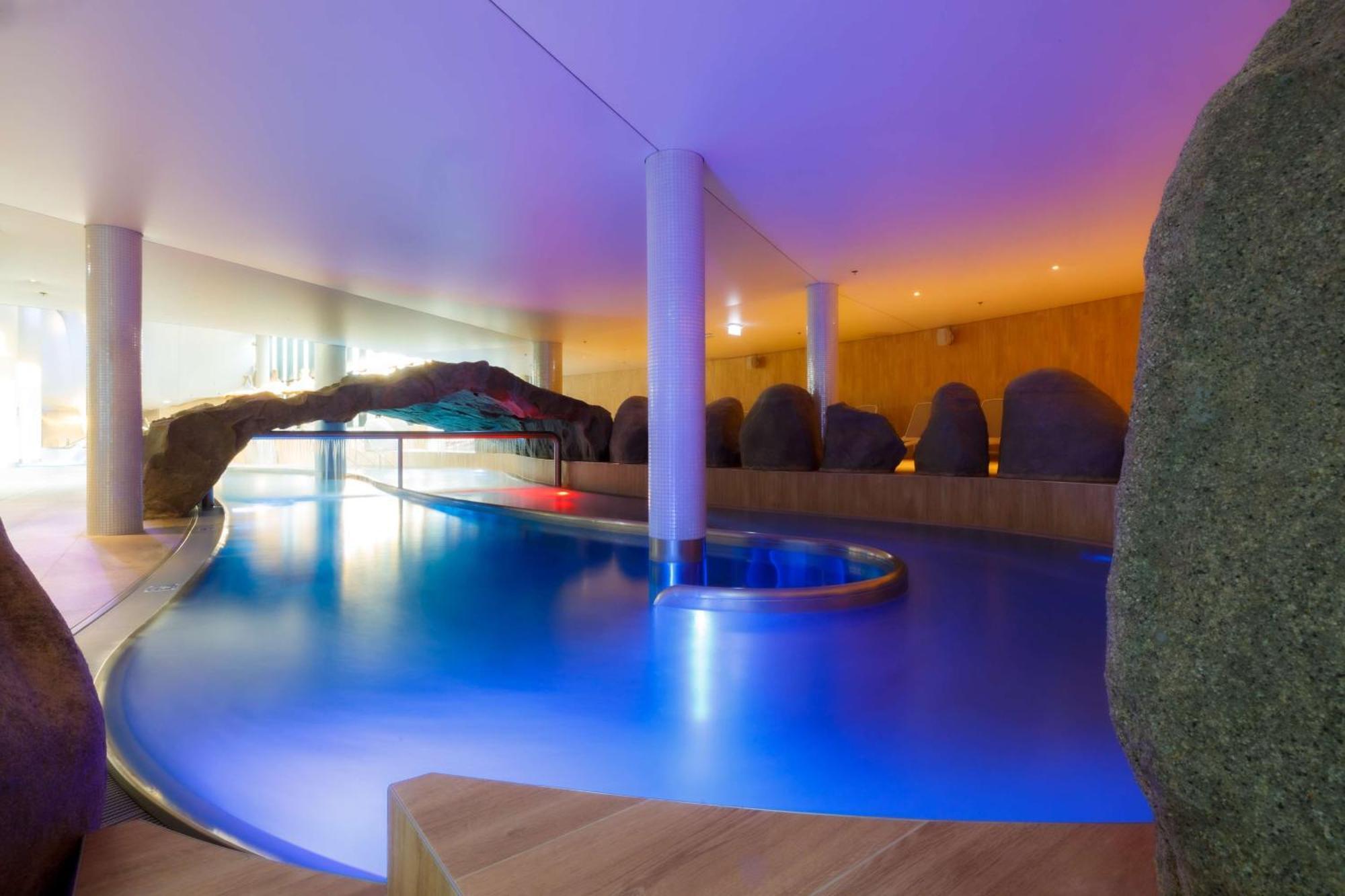 Radisson Blu Resort Swinoujscie Ngoại thất bức ảnh The photo showcases an elegant indoor swimming pool area. The pool has a flowing, organic shape and is illuminated with soft blue and purple lighting, creating a calming ambiance. Surrounding the pool are smooth, natural-looking stones and wooden ele