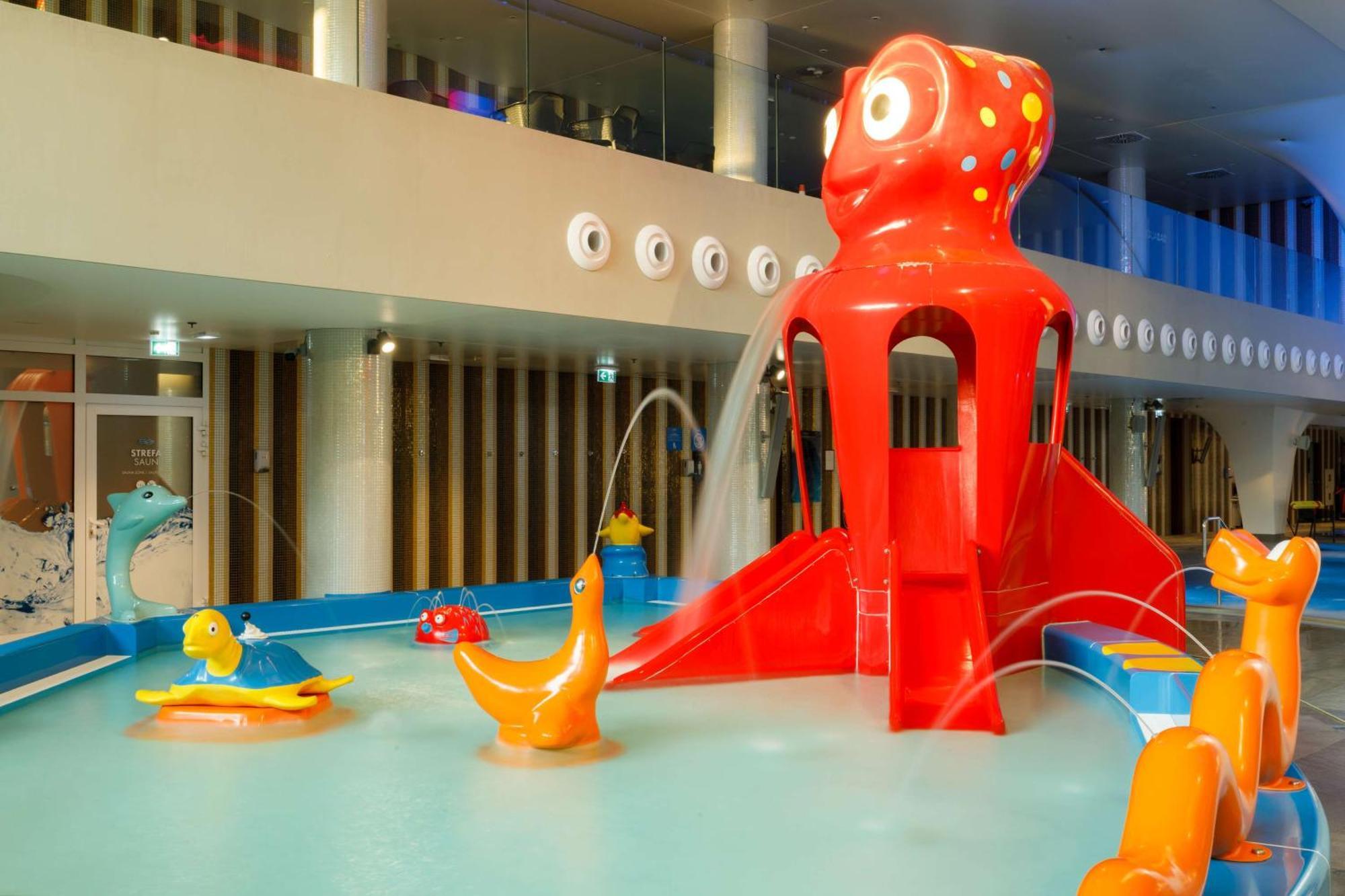 Radisson Blu Resort Swinoujscie Ngoại thất bức ảnh The photo shows a colorful indoor splash pad or water play area designed for children. Central to the scene is a large, bright red octopus structure, which has water fountains spraying out. Surrounding it are various playful, colorful water animals, 
